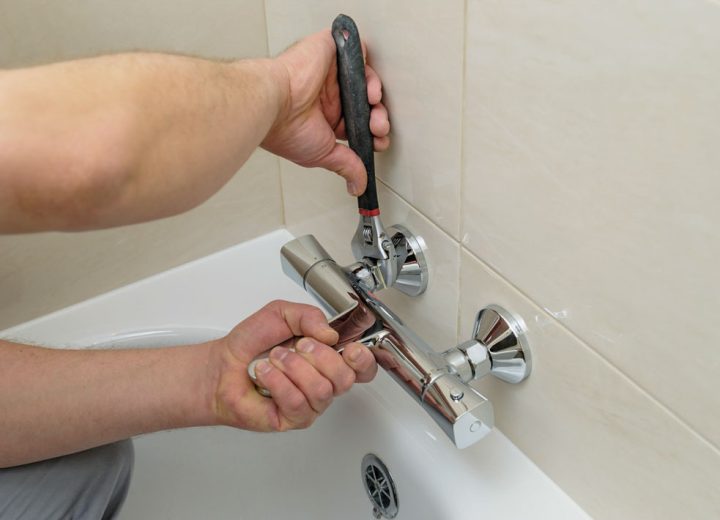 Installing faucet with thermostat. Man's hands are fixing bath tap into place.