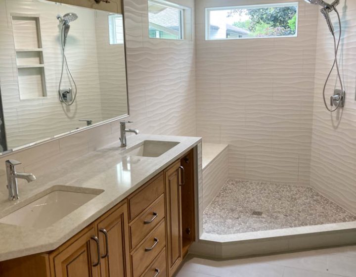 A modern bathroom with vanity cabinet with countertop and dual sink with faucet; a shower area with installed shower fixture and faucet